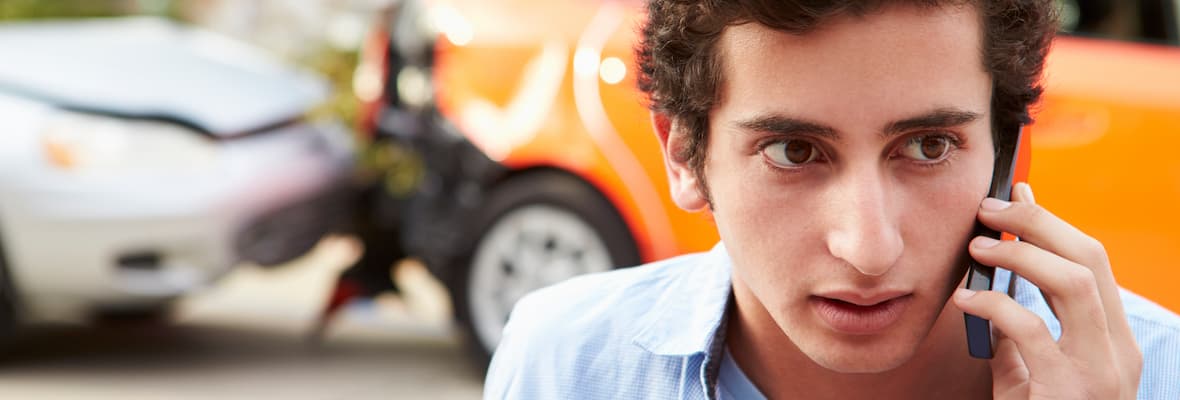 Young man calls his insurer in front of a car crash