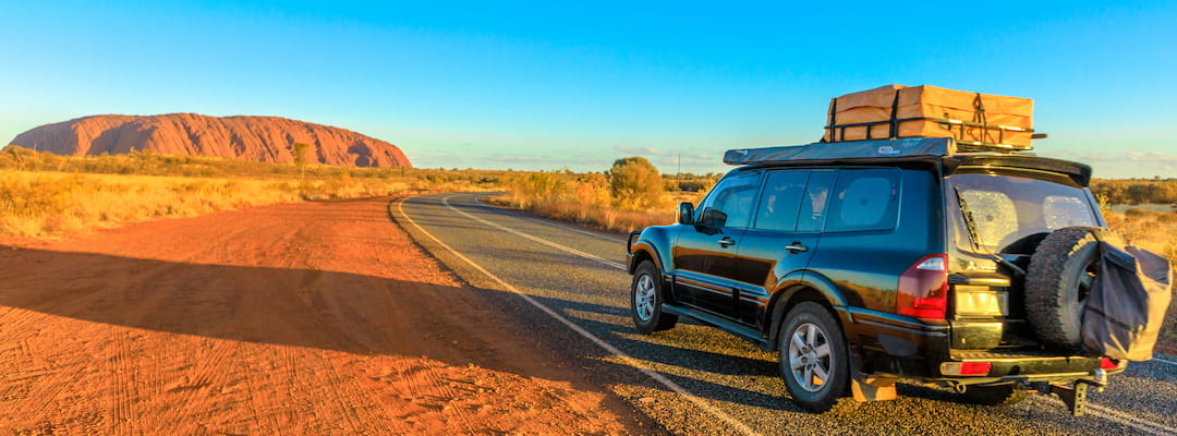 A four wheel drive vehicle travels along the road towards Uluru at sunset in the Northern Territory.