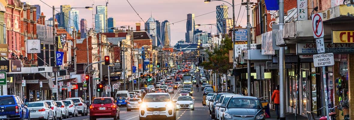 A busy Sydney Road in Brunswick in the early evening light with the Melbourne city skyline in the background.