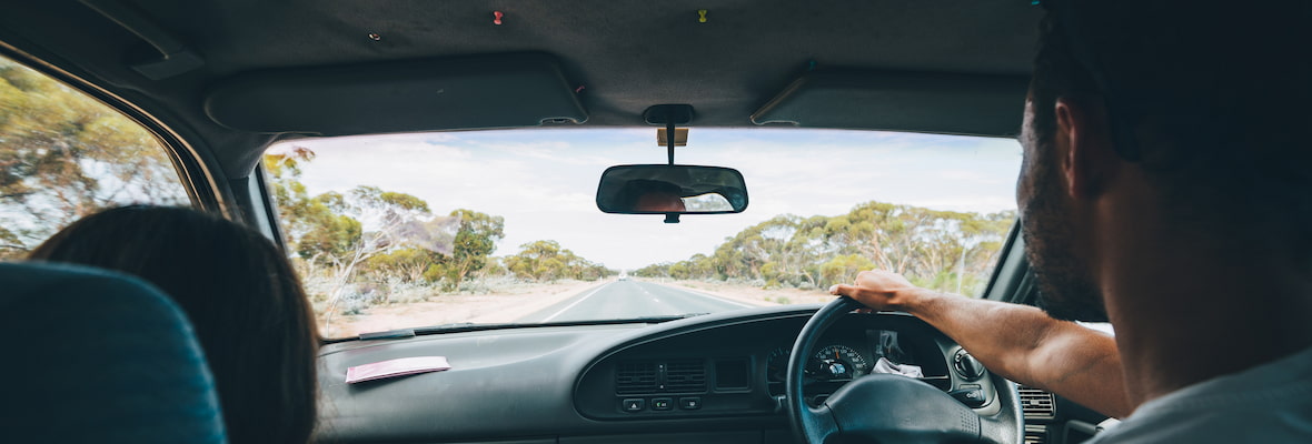 A man is drives a car with a female passenger across the Nullarbor Plain in Western Australia.