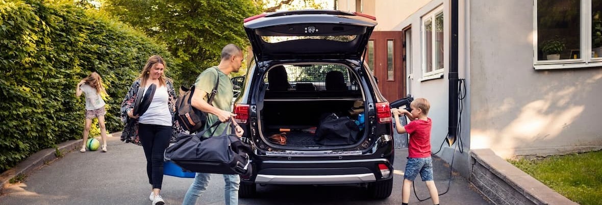 family packs luggage into family car boot while boy charges electric car