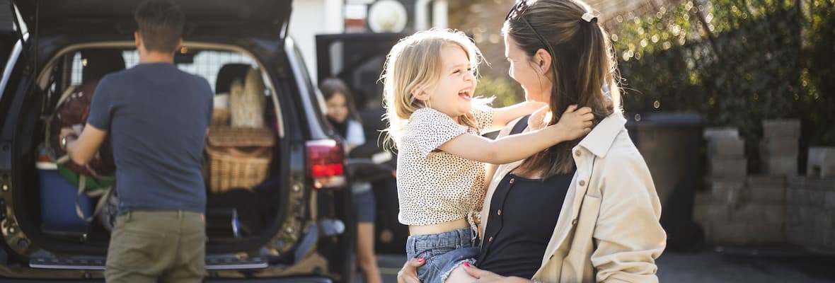 mother holding daughter while dad packs boot of family car SUV