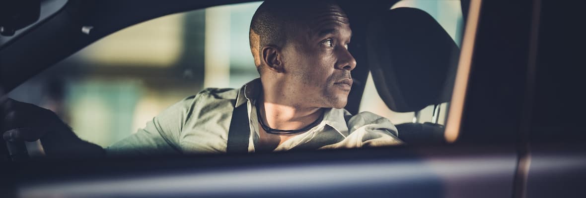 man looks nervously over shoulder while reversing car