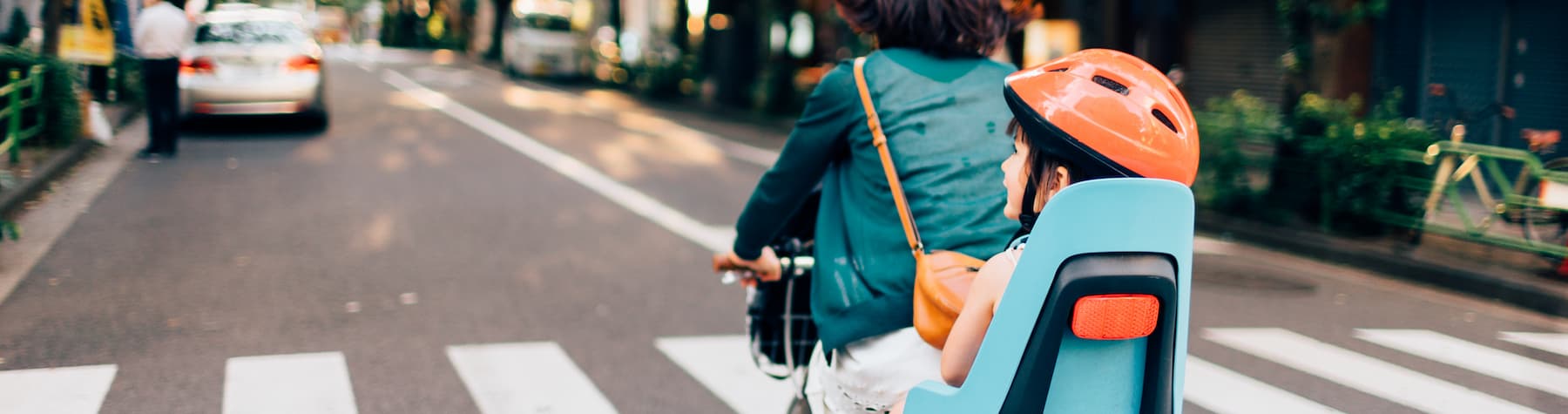 young boy with helmet in child seat of bike with mum riding through streets