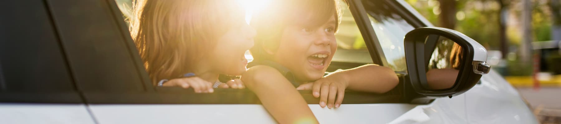 two children hanging out window of white car smiling