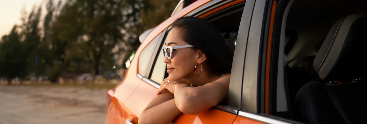 woman wearing sunglasses leaning out of back window of orange car