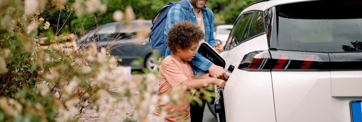 Father and son recharging white hybrid car