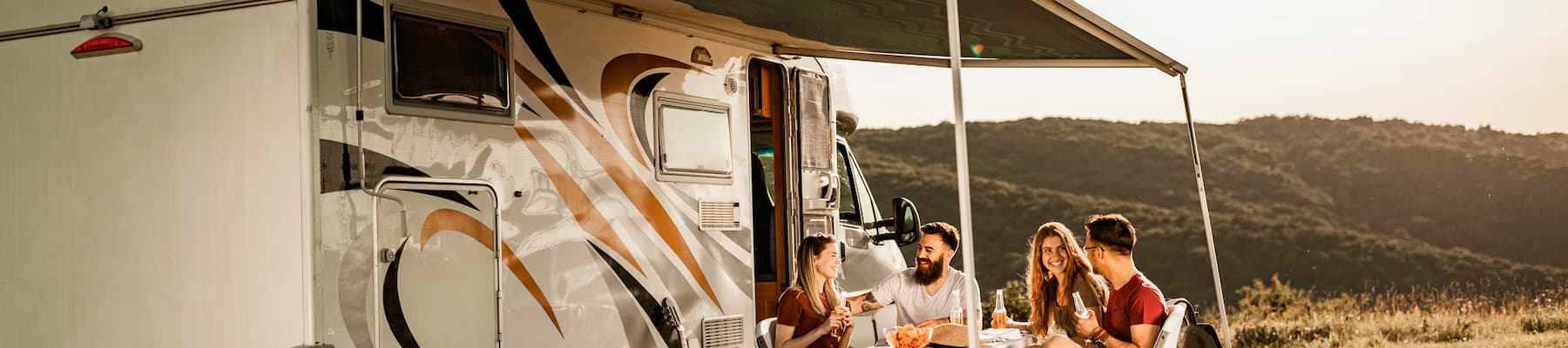 two couples laughing around table in front of caravan at sunset