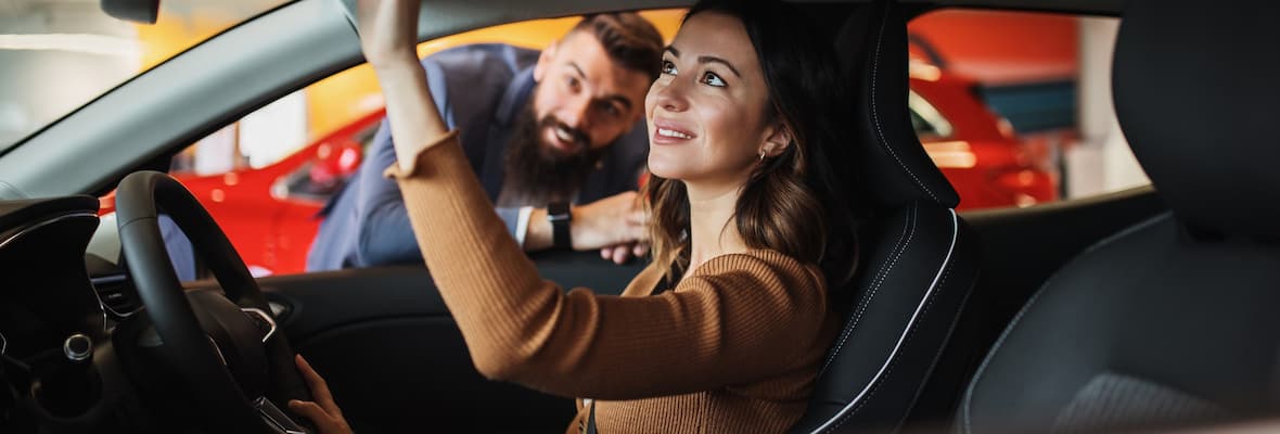 smiling woman sits in car while man looks through window