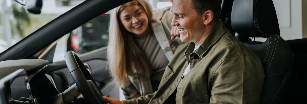 A man sits in the driver's seat of a new car in a dealership