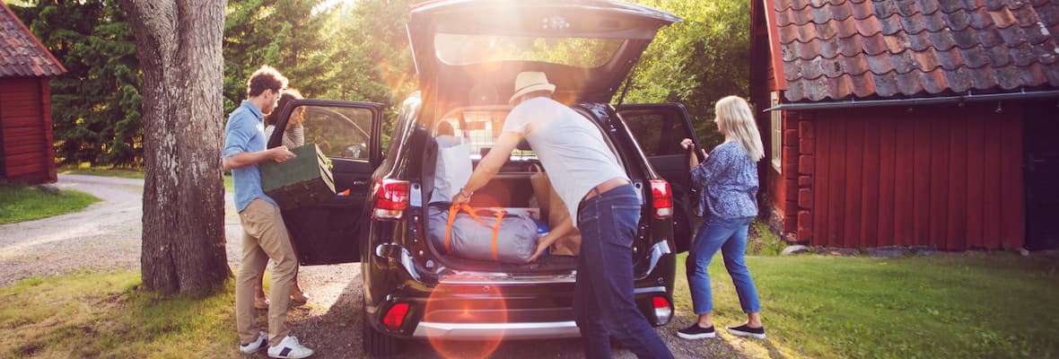 Four friends loading luggage into car on road on sunny day