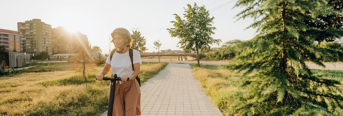 A woman wearing a helmet rides an electric scooter on a shared path in a park