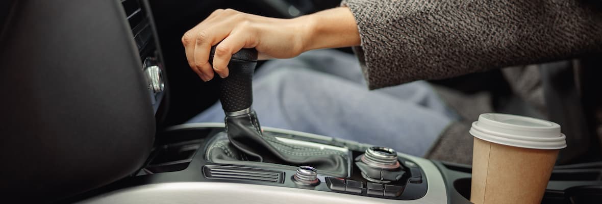 A woman changes speed by moving the leather gear selector forward in her car.