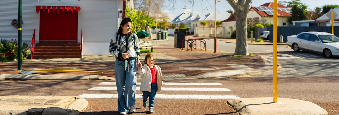 A mother and son hold hands while crossing the road together at a zebra crossing.