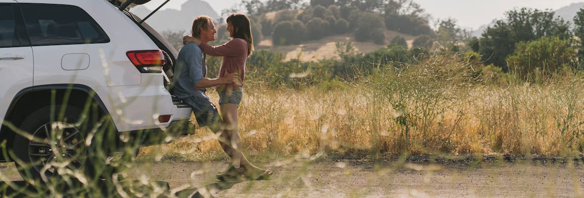 Young couple embraces at the back of an SUV in a rural grassy area