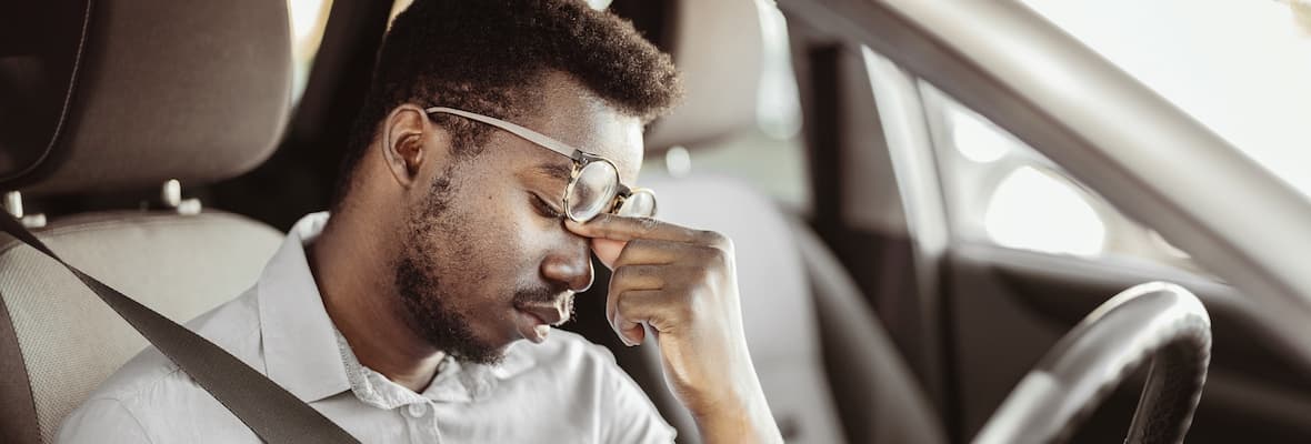 man rubbing eyes as driving car tired