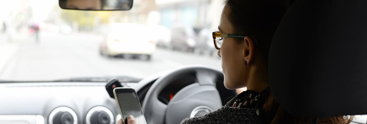 woman checks phone while driving in car