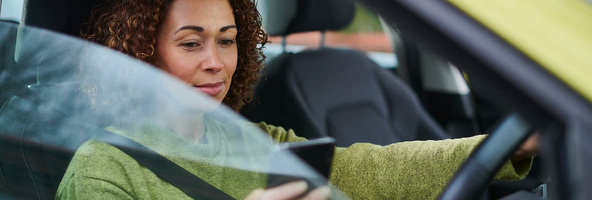 A woman uses her mobile phone (outside of its cradle) as she continues driving.