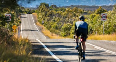 A cyclist rides downhill, passing green bushland on the road towards Sydney, New South Wales.