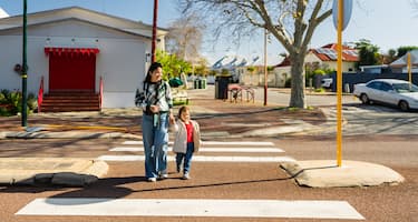 A mother and son hold hands while crossing the road together at a zebra crossing.
