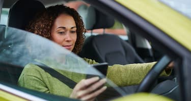 A woman uses her mobile phone (outside of its cradle) as she continues driving.