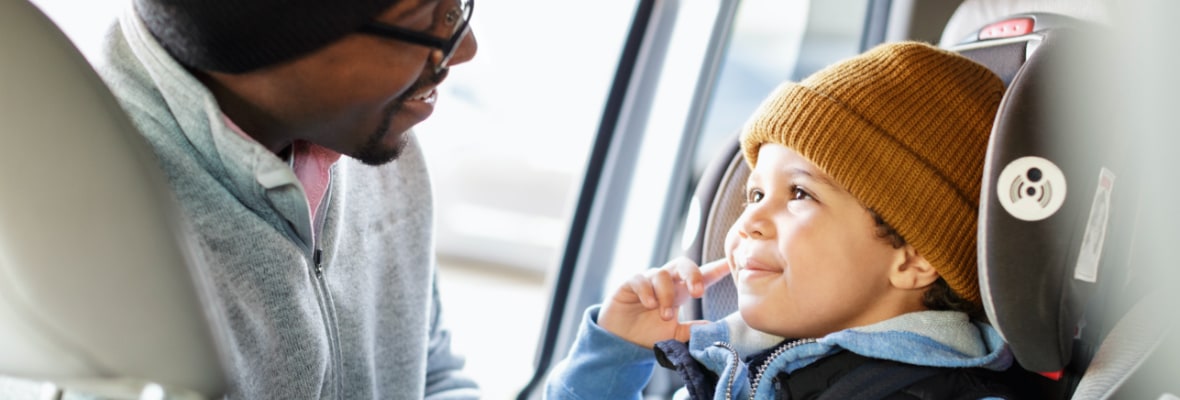 Father straps his young son into a forward-facing car seat before driving