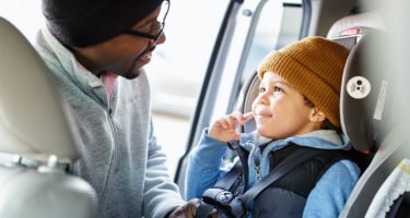 Father straps his young son into a forward-facing car seat before driving