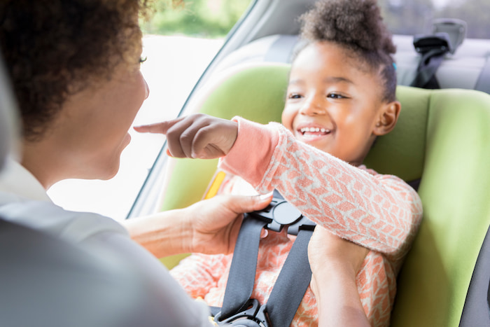 Woman secures her smiling daughter into a lime green ISOFIX approved car seat