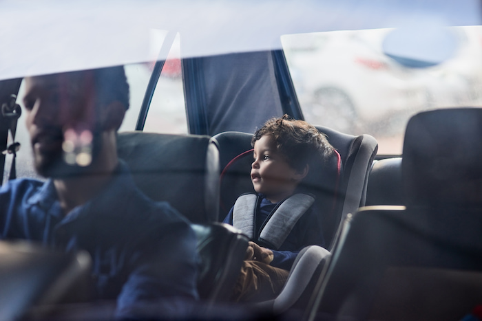 Young boy looks out of car window whilst securely fitted into car seat as his parent or guardian drives.