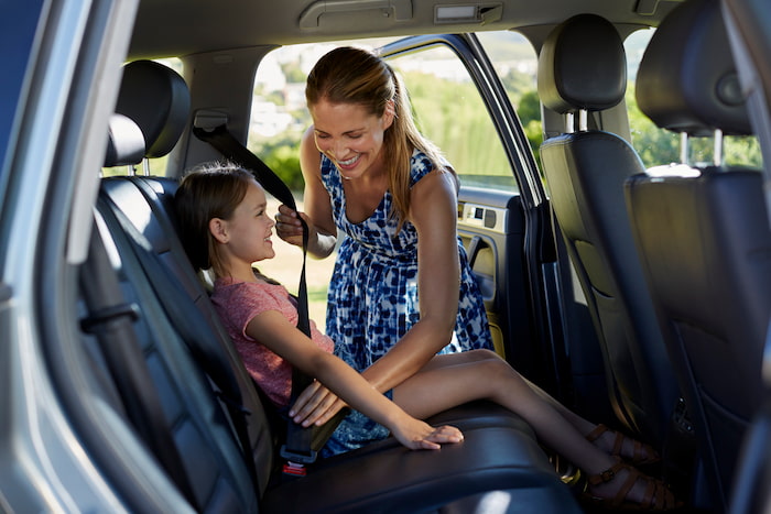Mother or guardian secures her young daughter with seat belt into backseat of car
