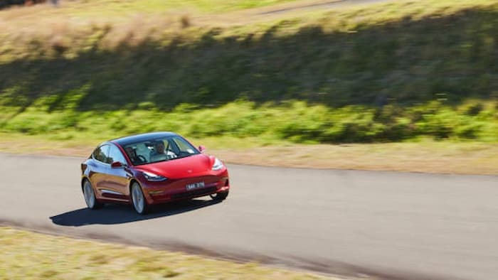 Red Tesla Model 3 driving along road near green grass in countryside