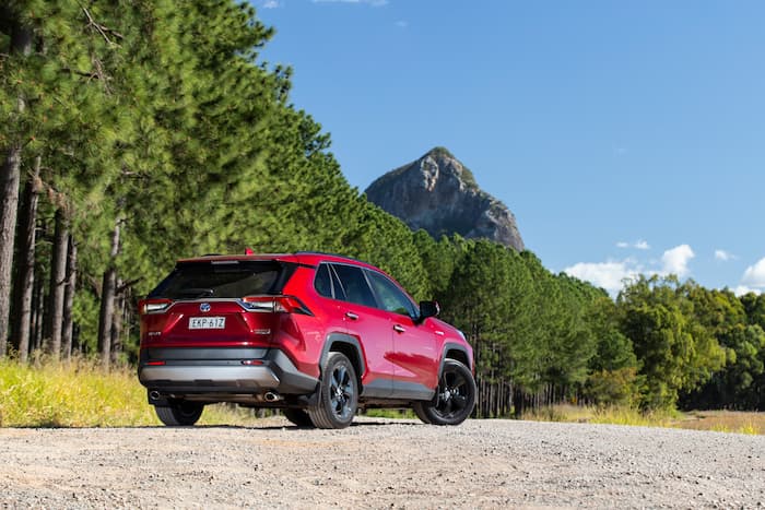 Red RAV4 cruiser hybrid car parked on dirt road with mountain in the back