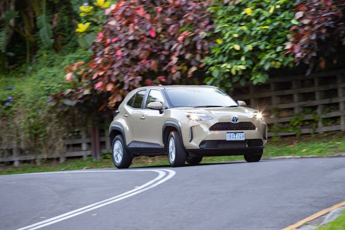 Cream Toyota Yaris Cross Hybrid driving on road with greenery