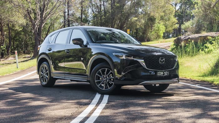 Black Mazda CX5 is parked across a road outside a park