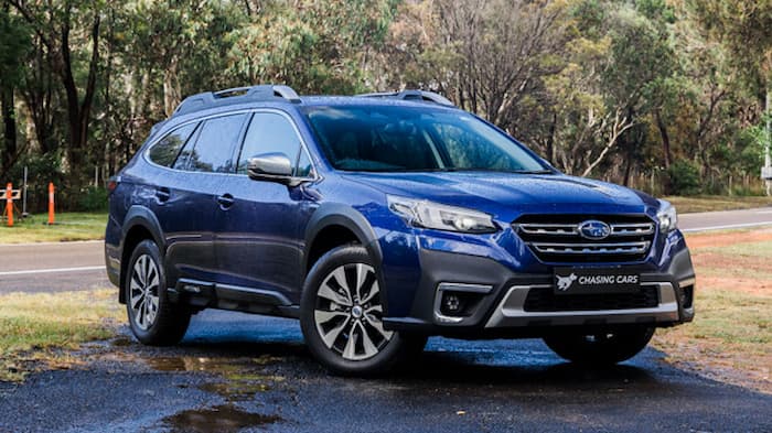 blue Subaru Outback parked on wet road outside in front of grass
