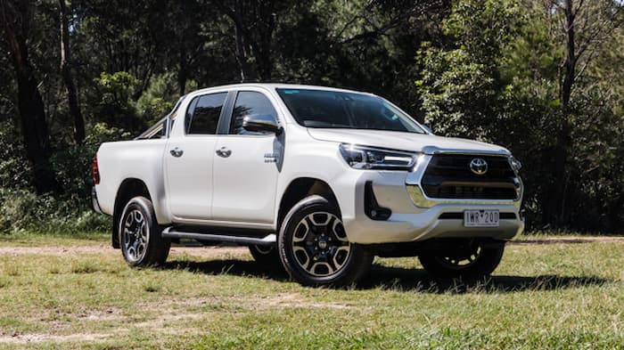 white Toyota Hilux parked on grass outside in front of trees