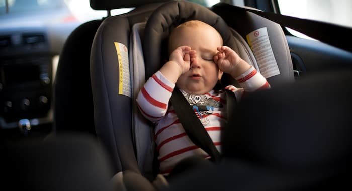 A baby rubs their eyes in a child's car seat