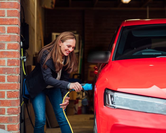 Woman uses a dedicated ev cable to charge a red car in her garage
