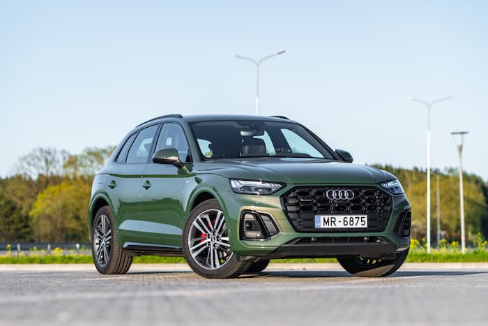 Green Audi Q5 drives on a paved road near green trees