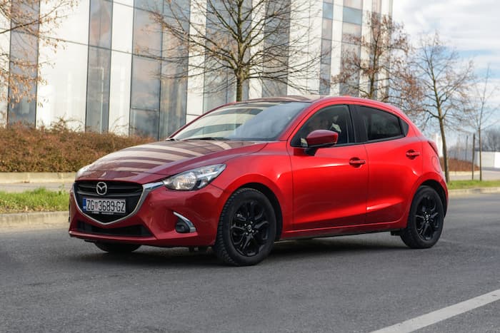 Red Mazda 2 drives alongside an office building outside