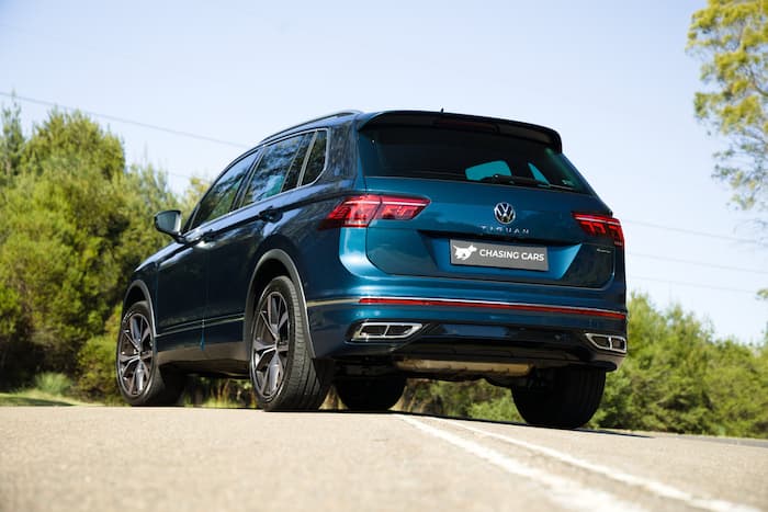 Blue Volkswagen Tiguan R is parked across a road surrounded by trees