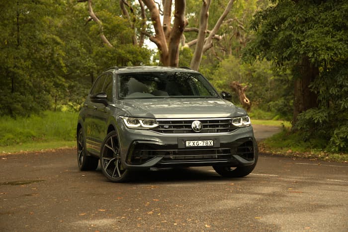 Green Volkswagen Tiguan is parked in the middle of the road surrounded by greenery
