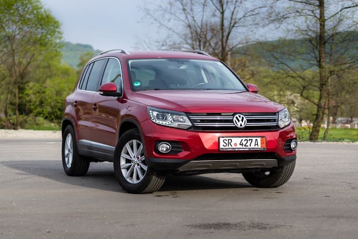 Red Volkswagen Tiguan Allspace Adventure is parked in front of green grass and trees