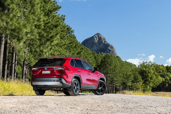 red RAV4 cruiser hybrid car parked on dirt road with mountain in the back