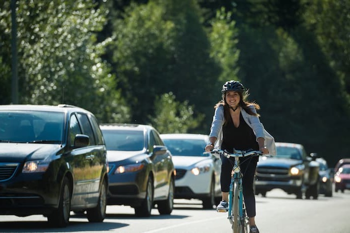 A woman cycles past motorists in the bike lane of a busy road.