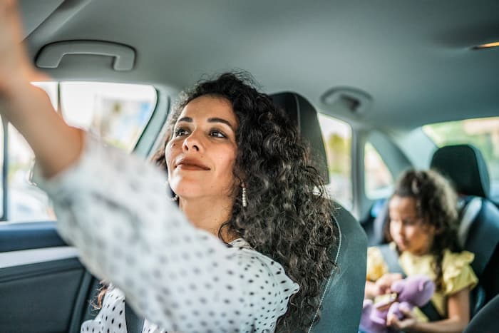 A woman adjusts her mirrors to check for blind spots before driving with her young daughter.
