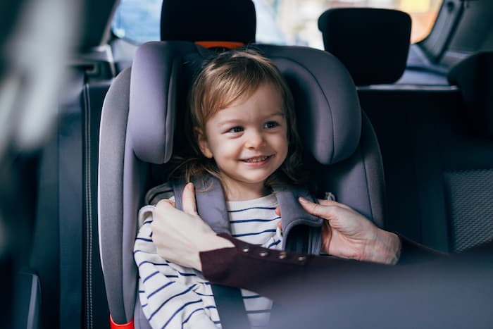 A young girl is buckled and fastened into her car seat by her mother using a seat belt.