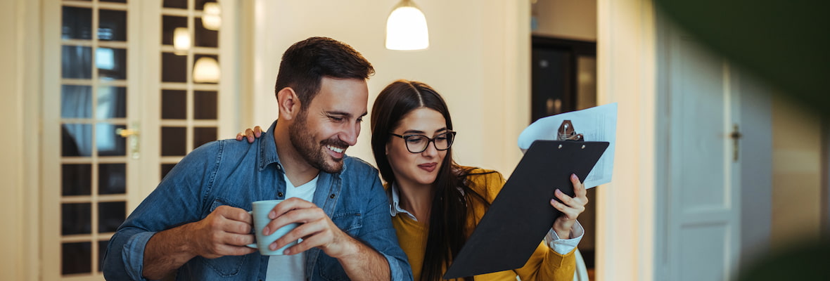 A young couple are happily looking over a checklist on a clipboard while having coffee.