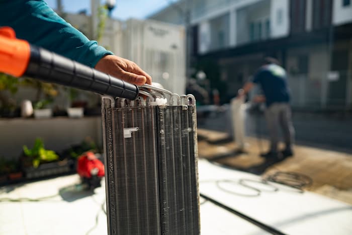 A man pours water on dirty evaporator coils from an air conditioner outside his home.