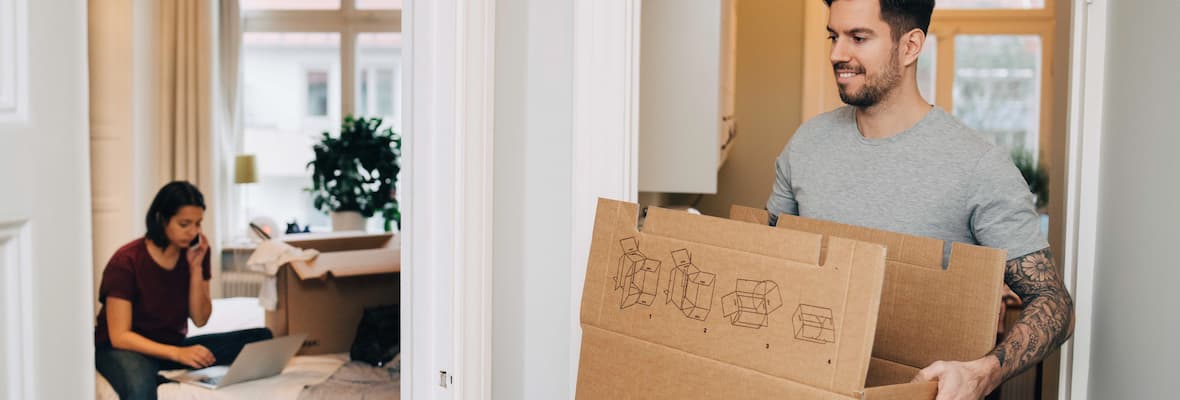 A man packs boxes while his partner checks their moving budget